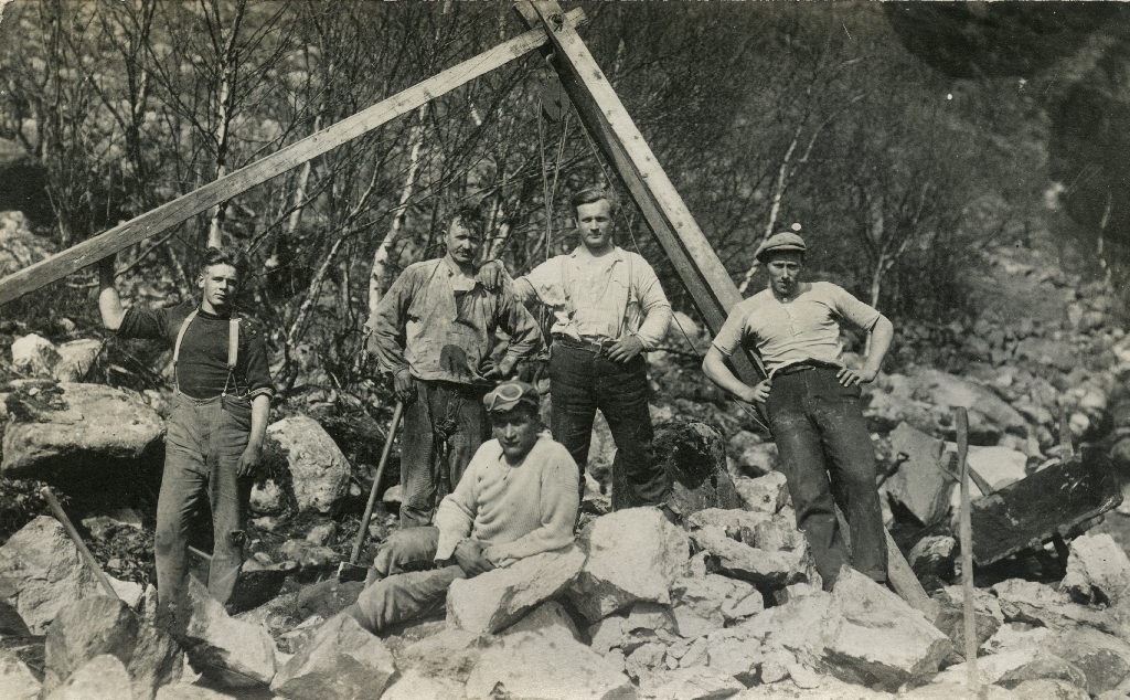 Fem unge arbeidarar attmed ein steinbukk. Biletet er tatt under byggjing av Oltedalsvegen ved Ytre Lima i 1924.