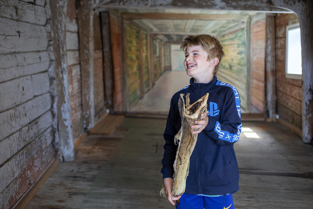 En glad gutt holder en tørrfisk i hendene i et av de vakre rommene på Norges Fiskerimuseum