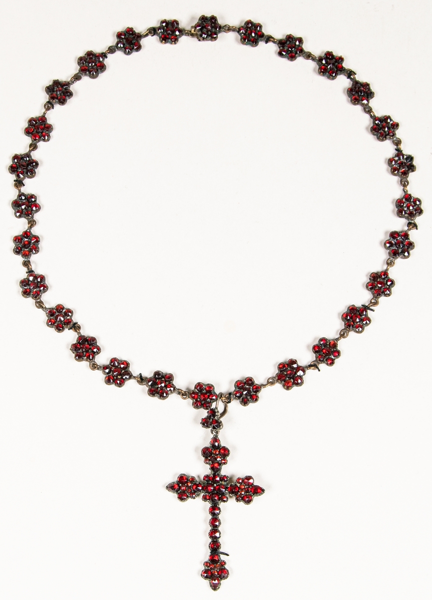 Halsband, gul metallegering med röda stenar, troligen granater. Från halsbandet hänger ett kors i samma material.