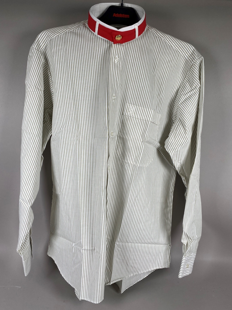 Hvit skjorte med lysegrå striper. Rødt bånd i halsen og brodert posthornlogo på brystlommen. Skjorten er langermet og er i størrelse "small".