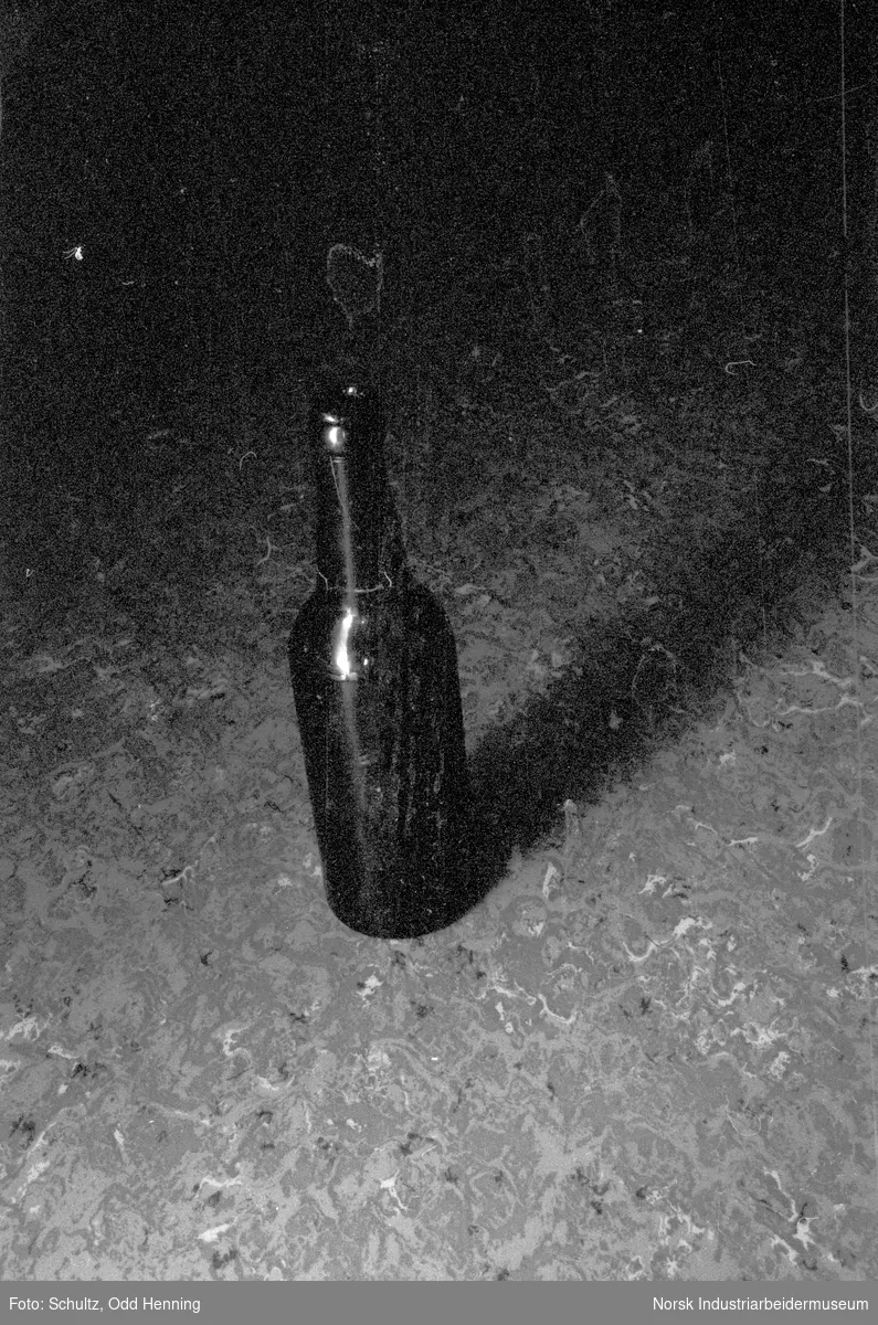 Flaske i farget glass som står på gulvet.