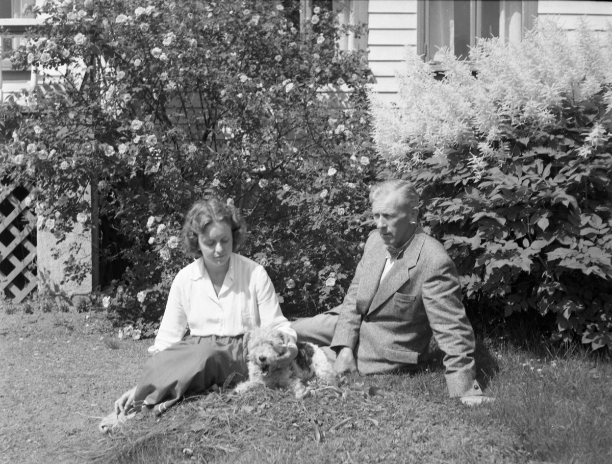 En mann og en kvinne sittende på plen sammen med en hund.