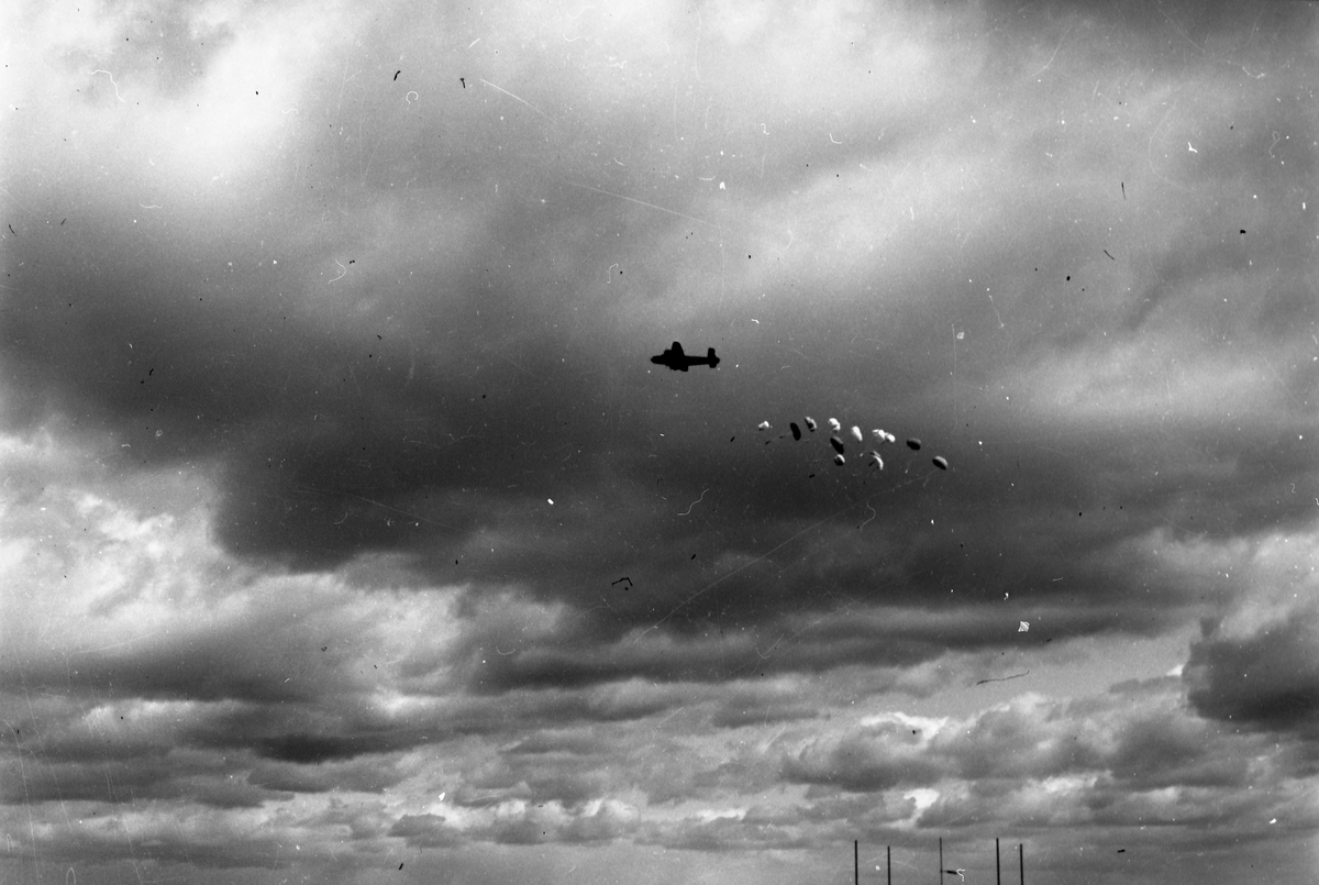 Et bombefly ved navn Consolidated B-24 Liberator slipper ut innhold fra flyet. En rekke fallskjermer er spred utover himmelen.