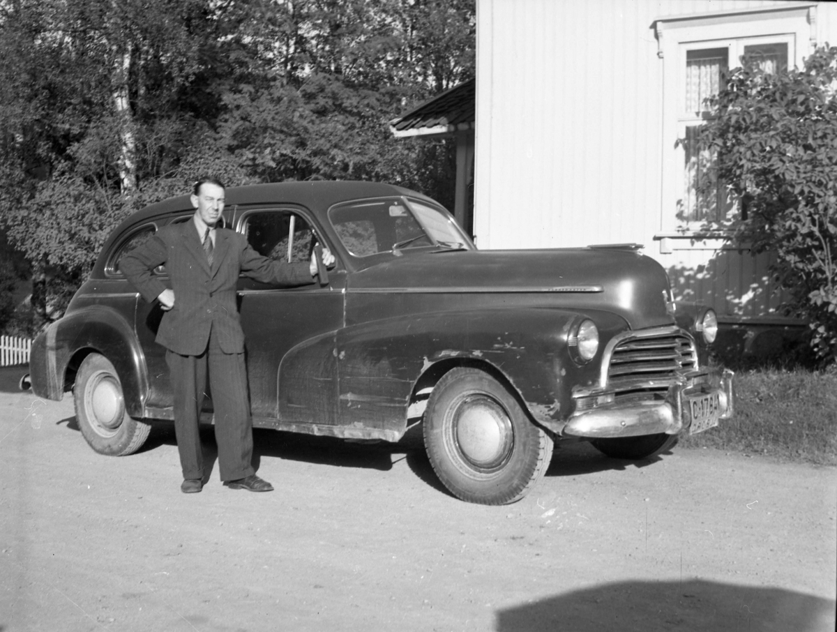 En mann i dress stående ved en drosje med skiltnummer C17641.