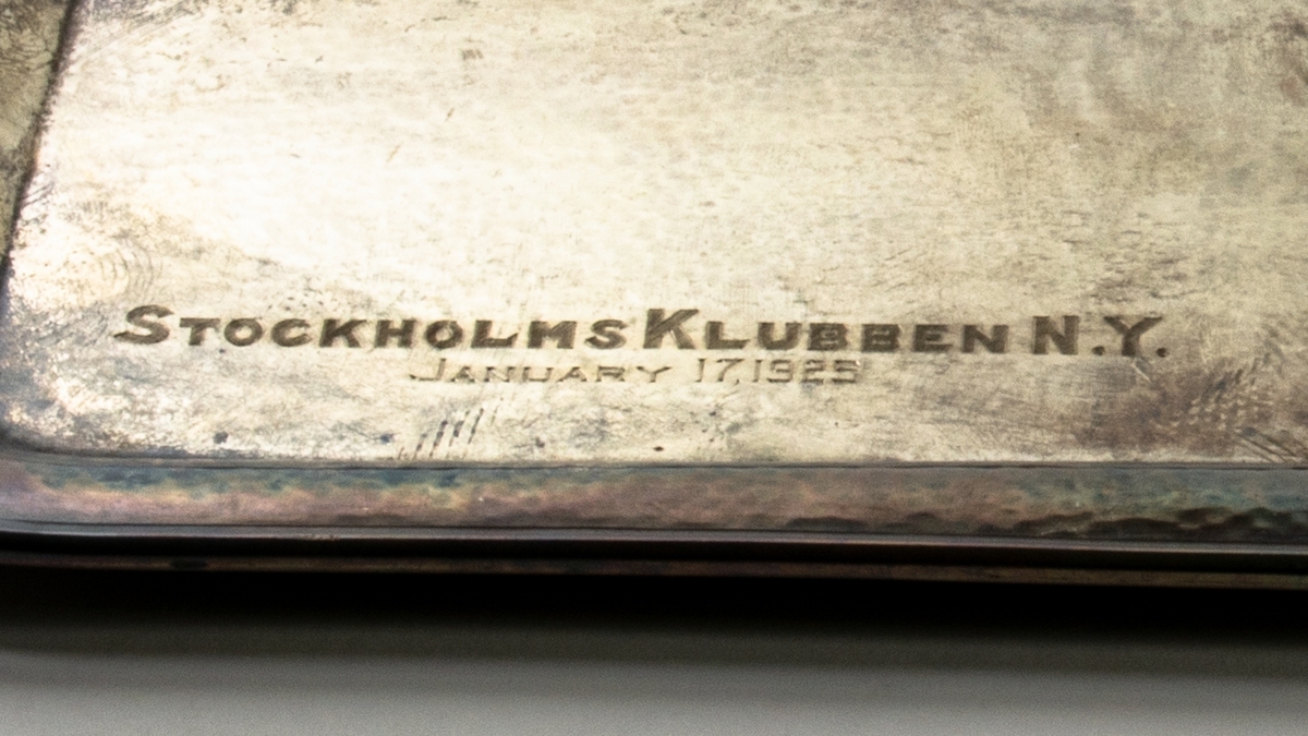 Serveringsbricka med handtag, tillverkad av sterlingsilver. 
Graverad text: "Stockholmsklubben n.y. January 17, 1925".