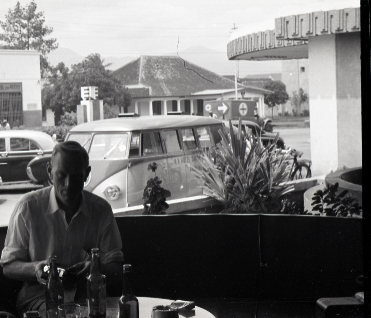 Mann holder i et kamera ved et bord. Sansynligvis i kantina på Hotel Savoy Homann, Bandung, Indonesia.