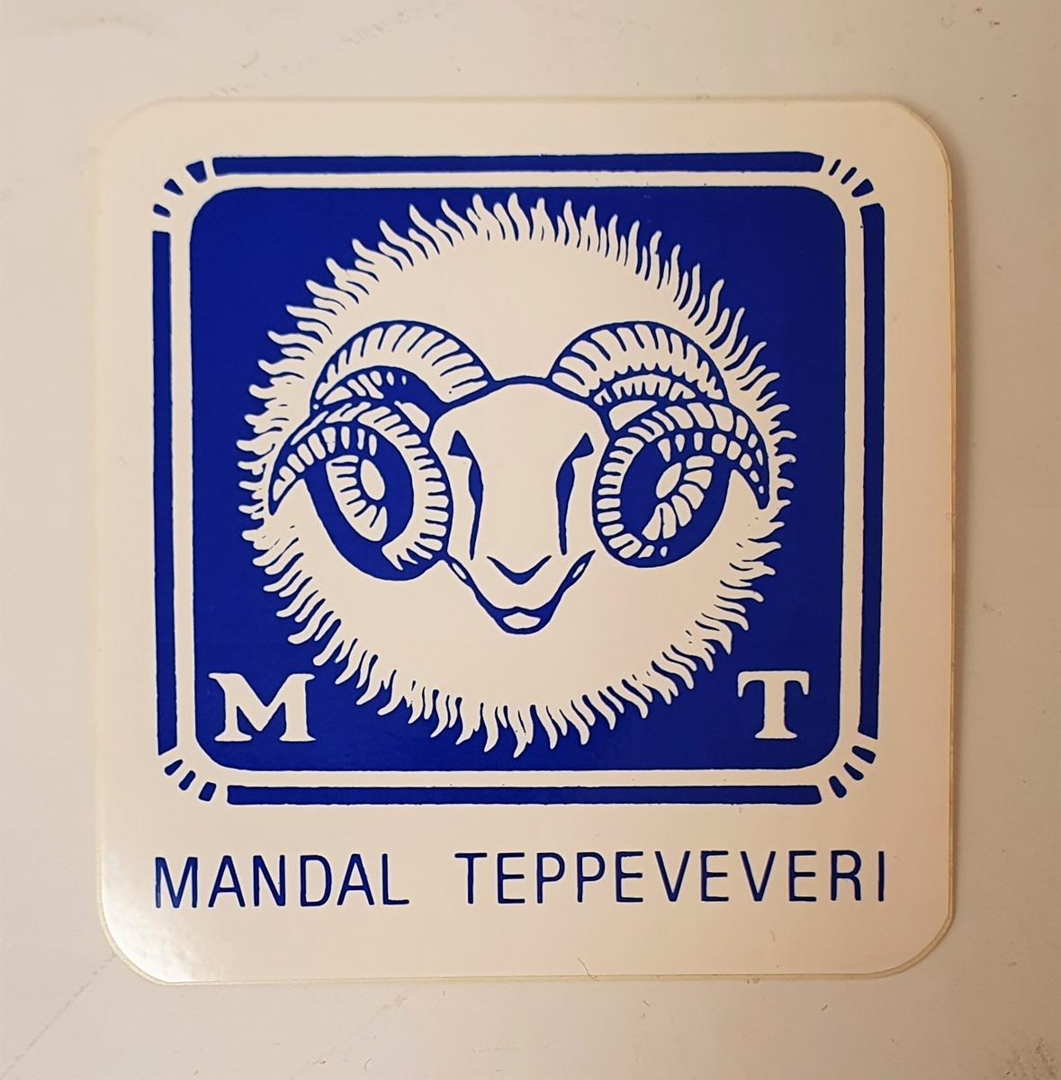 Klistermerke med bedriftsnavn og logo for Mandal Teppeveveri.