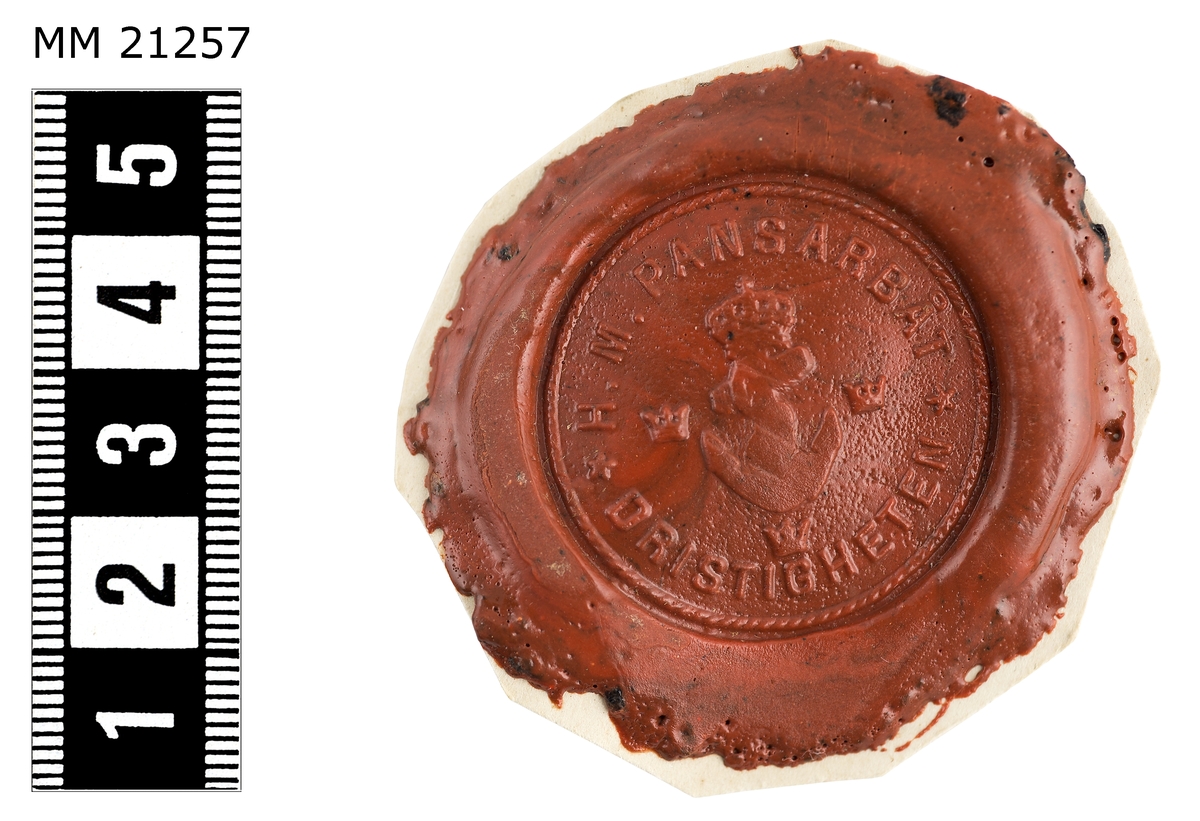 Sigillavtryck av rött lack på papper. I mitten krönt stockankare omgivet av tre kronor. Längs kanten text: "H.M. pansarbåt Dristigheten".