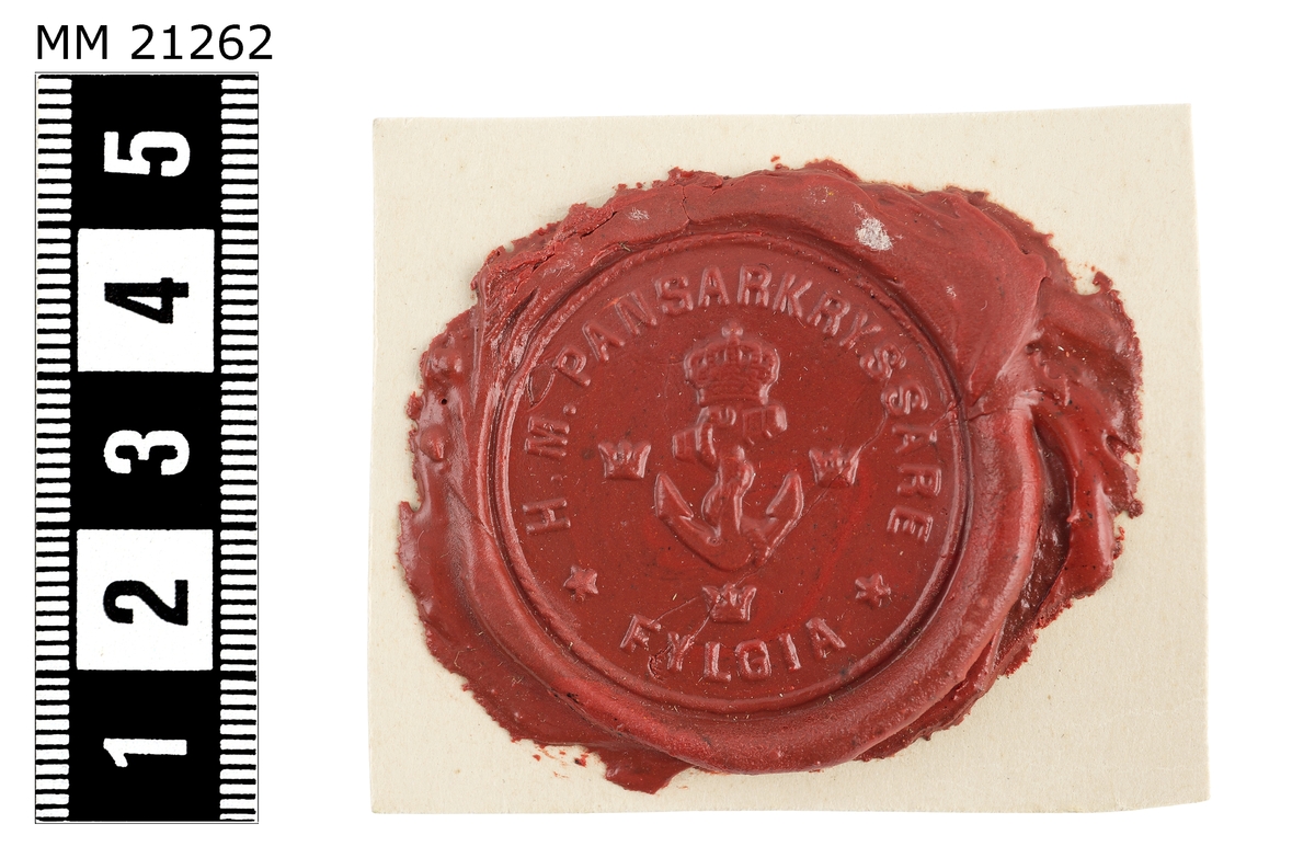 Sigillavtryck av rött lack på papper. I mitten krönt stockankare omgivet av tre kronor. Längs kanten text: "H.M. pansarkryssare Fylgia".