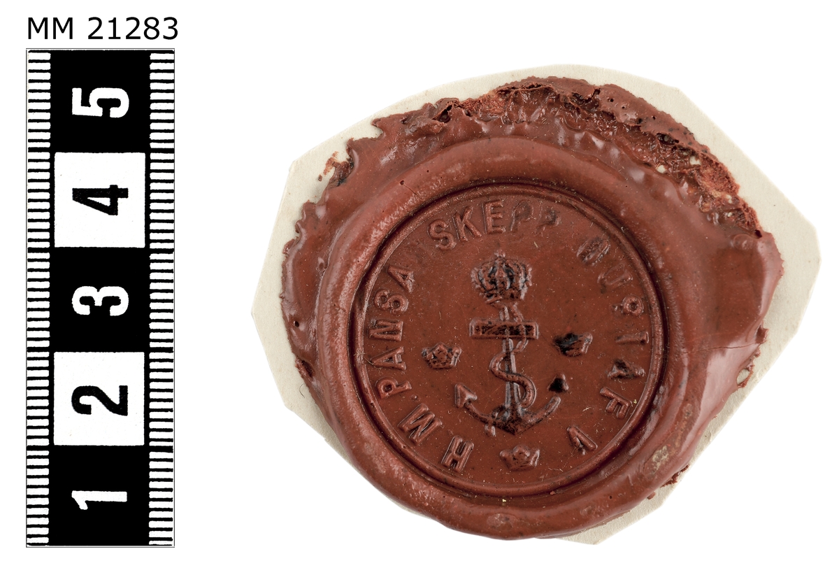 Sigillavtryck av rött lack på papper. I mitten krönt stockankare omgivet av tre kronor. Längs kanten text: "H.M. Pansarskepp Gustaf V".