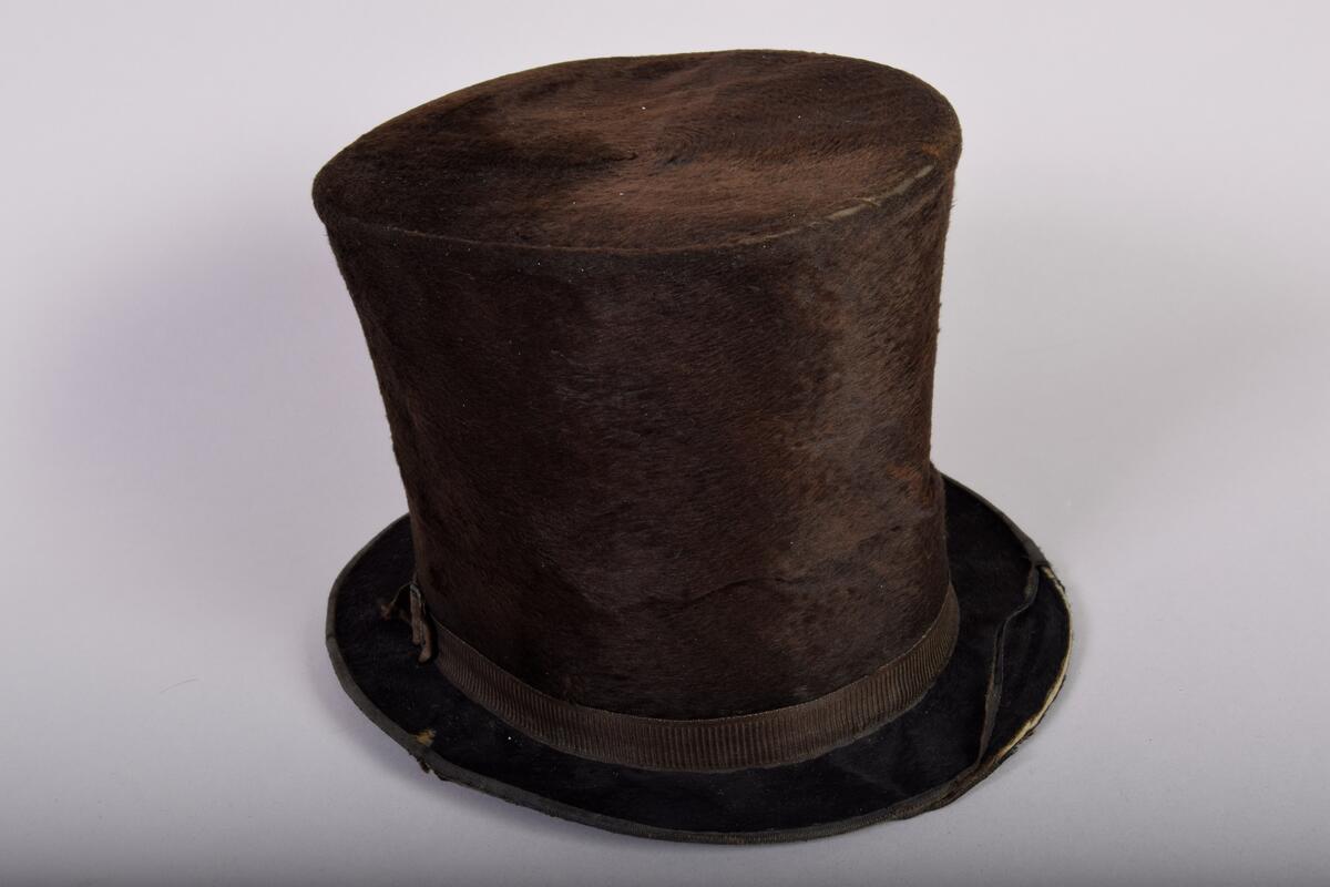Hög hatt av svart felb. Foder av tunt skärt siden, gul läderrem med gult sidenband. Från 1800-talets början. Firmamärke: Manufacture de ---, Paris. 