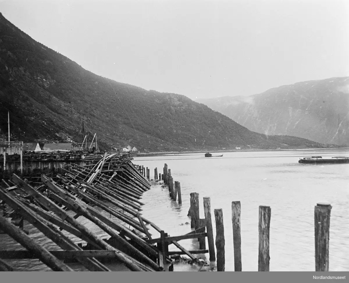LKABs kullkai etter stormen i 1901. Til venstre ses kaien med påler og stokker som støtter opp mot kaien. Til høyre ses havna med båter. I bakgrunnen en del av Fagernesfjellet og Fagernes. En del av Ankenesfjellet forsvinner innover mot Beisfjord.