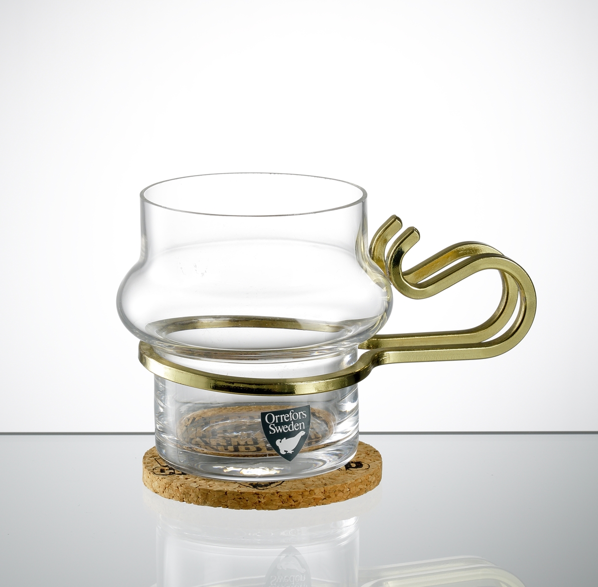 "Varm Kall", formgiven av Lindau & Lindekrantz. Glas för glögg, mocka, sherry. Cylindrisk form med vulst på kupans mittdel. Öra i mässing. Tillhörande underlägg i kork.