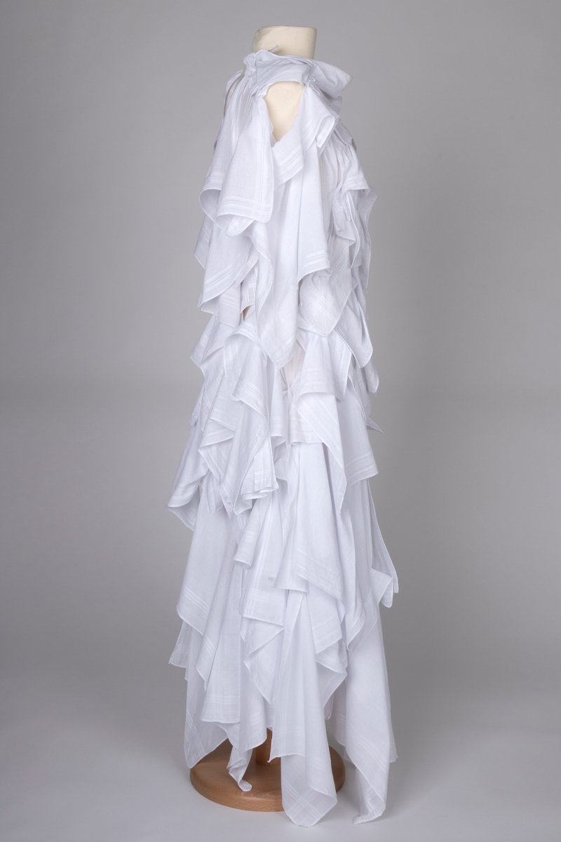 Hvitfarget kjole bestående av bomullslommetørkler, utført i "Similar Draping"-teknikk. Plagget har et sterkt dekonstruert preg, hvor man skulpturelt danderer tørklene rundt bærerens kropp.