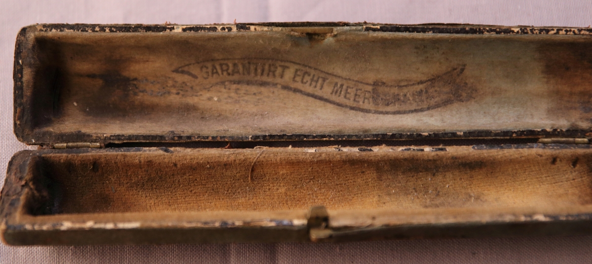 Etui i läder med delar av mässing. På insidan står ”Garantirt echt meer(…oläsbart)”. Munstycket i snidat trä.