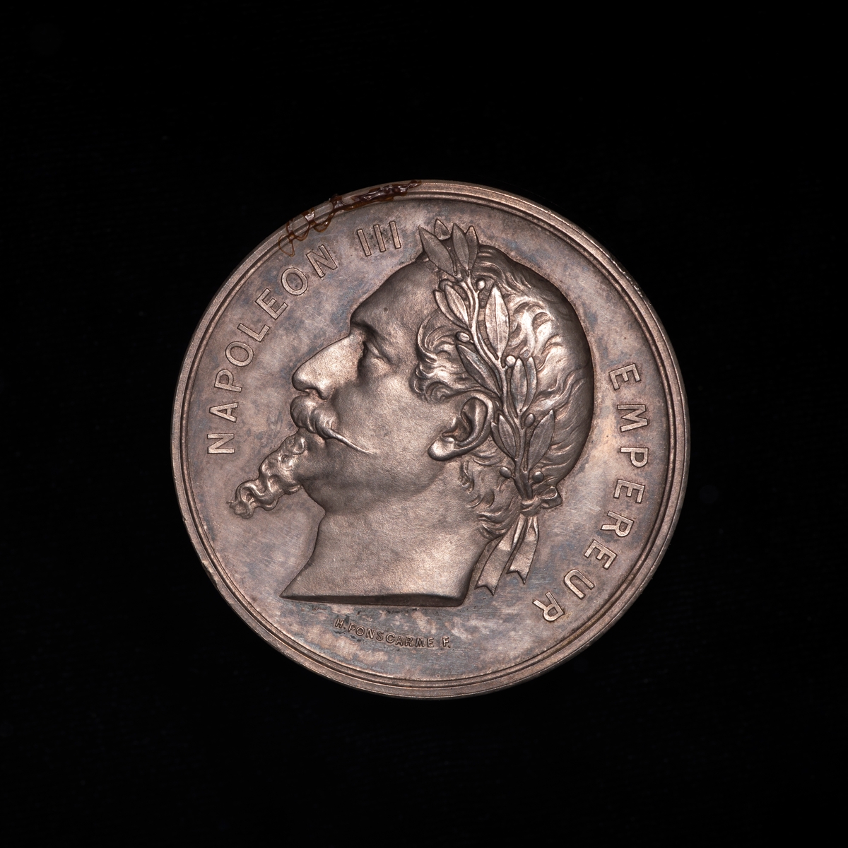 Sølvmedalje fra utstilling i Paris 1867. På advers portrett møt venstre av Napoleon III. På reversen innskrift.
