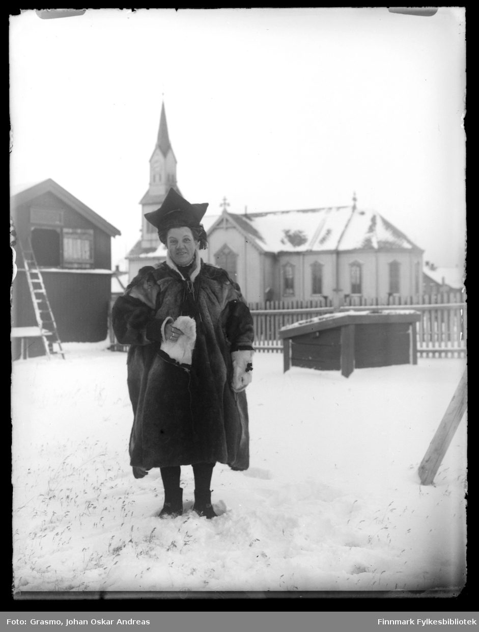 En person i pesk, stjernelue og skinnvotter fotografert ute i snø. Vardø kirke i bakgrunnen.
