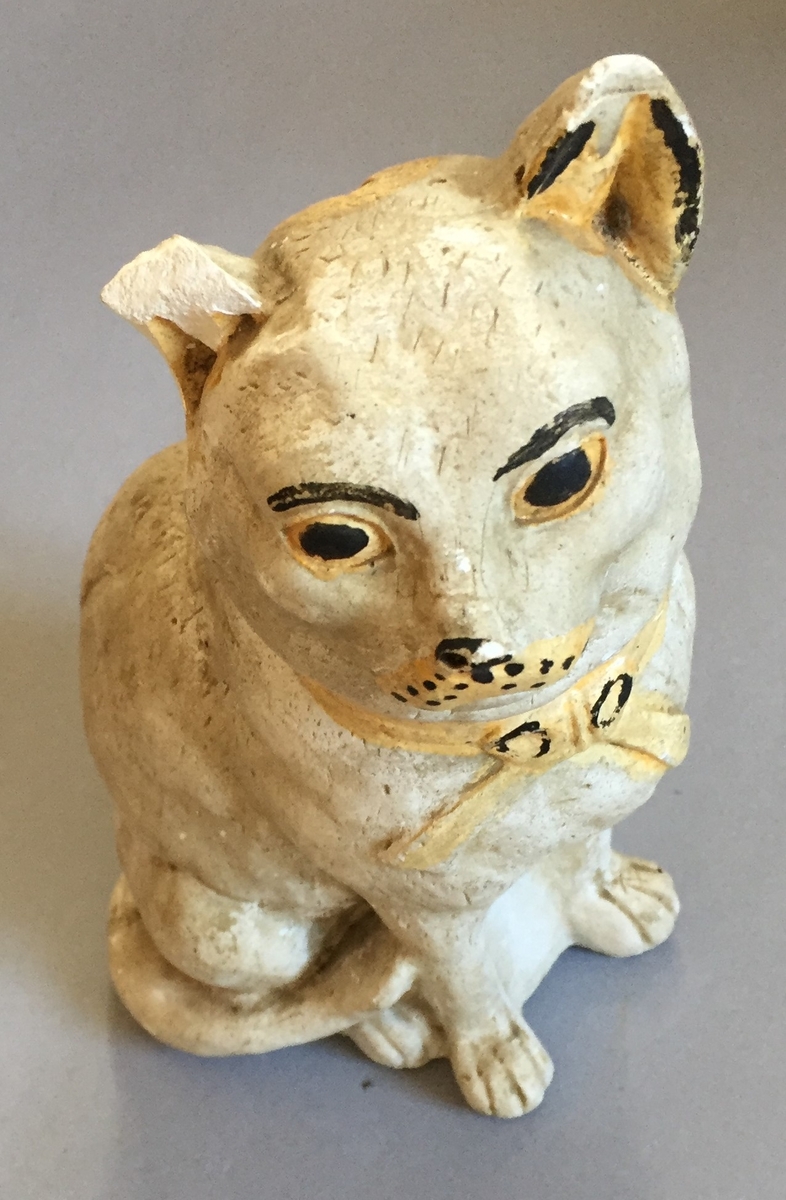 Figur i steintøy, forma som ein katt. Opningbak på hovudet til å putte inn pengar. Sparebøsse.