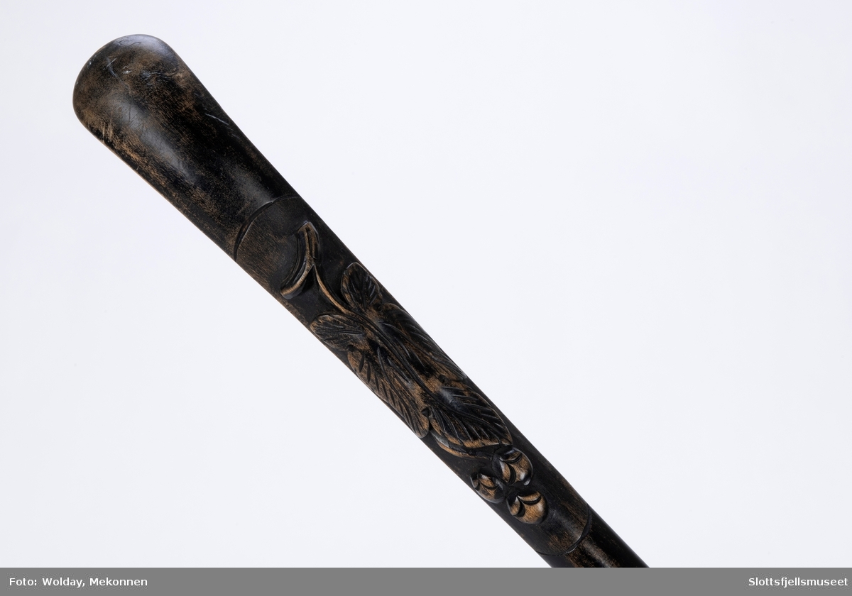 Spaserstokk som ser ut som en sammenslått  paraply i etui. Svart stoff etui med svart sløyfe nær håndtaket. Utskjæring på håndtaket.