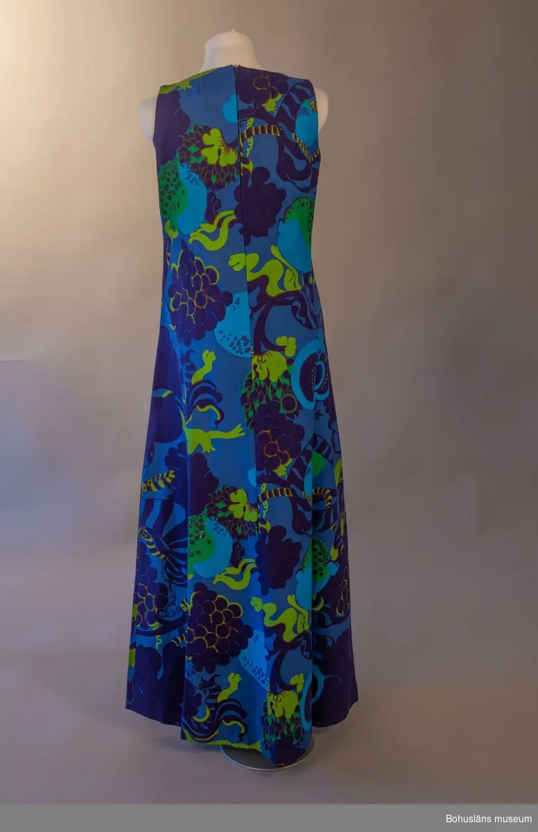 Stormönstrad lång klänning i styvt bomullstyg med blå botten. Rak passorm med något utsvängande kjolparti. Sydd av fyra avlånga våder.