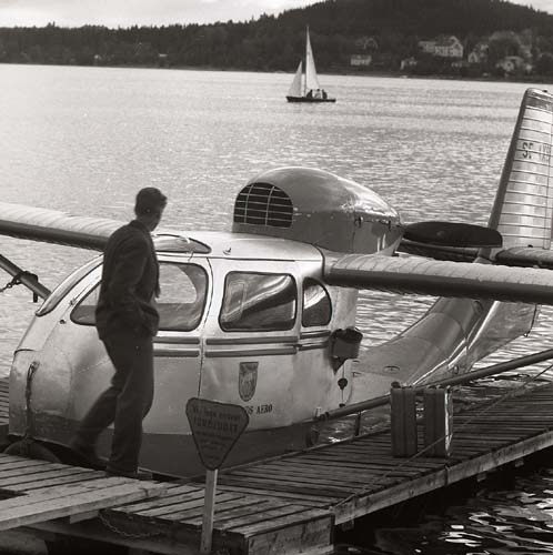 Amfibieflygplan modell Republic RC-3 Seabee har landat på sjö i Östersund, 6 augusti 1959. På bryggan står en man med bränsle. Jämtlands Aero, registreringsnummer SE-AXB.