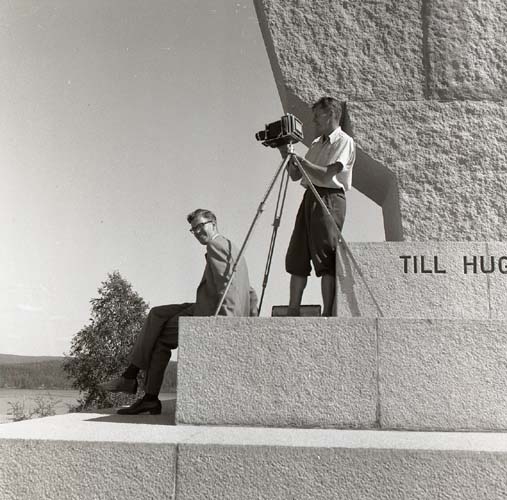 Örnmonumentet med en örn av brons på ett monument av granit av Jussi Mäntynen, 13 augusti 1955. Hilding och Arne D. vid foten av munumentet. Hilding står bakom en kamera på stativ. Värmlandsresan 11-18 augusti 1955.