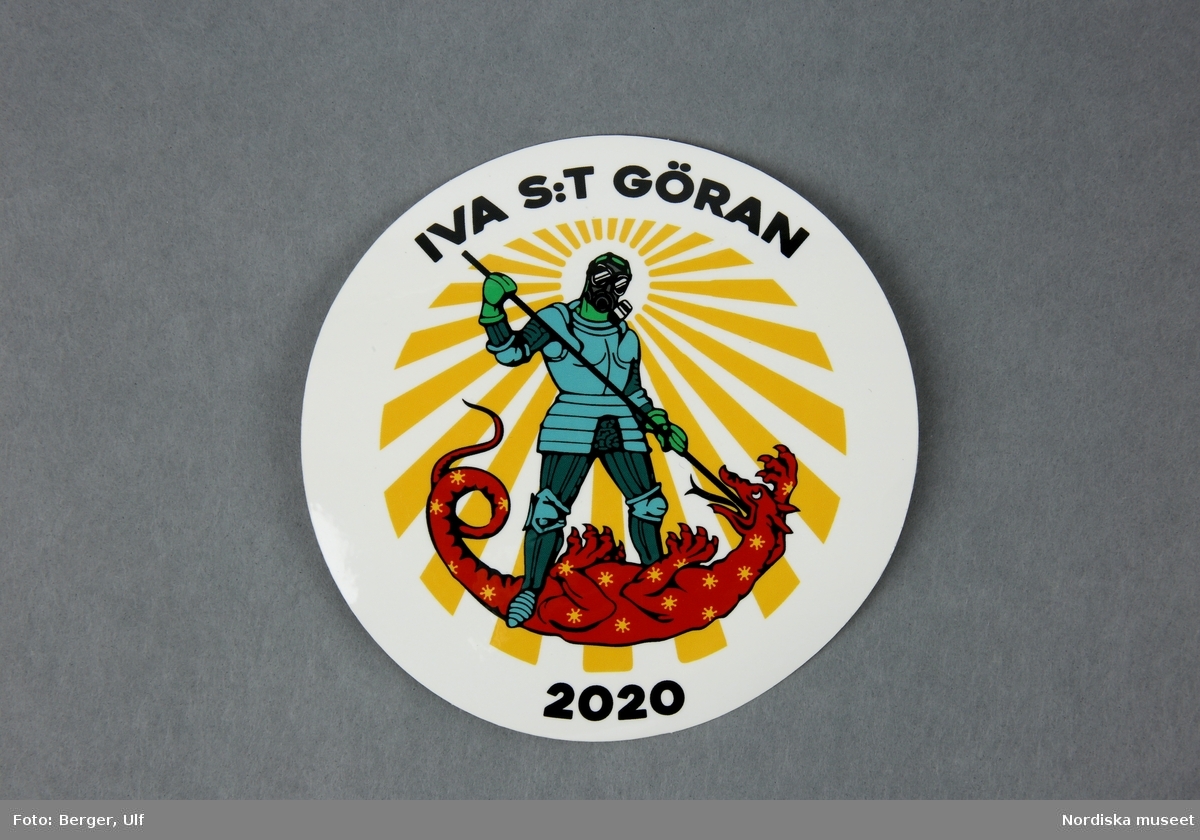 Runt klistermärke i vit färg med motivet en riddare (S:t Göran) som dräper en röd drake infekterad med coronavirus samt texten ”IVA S:t Göran 2020”.