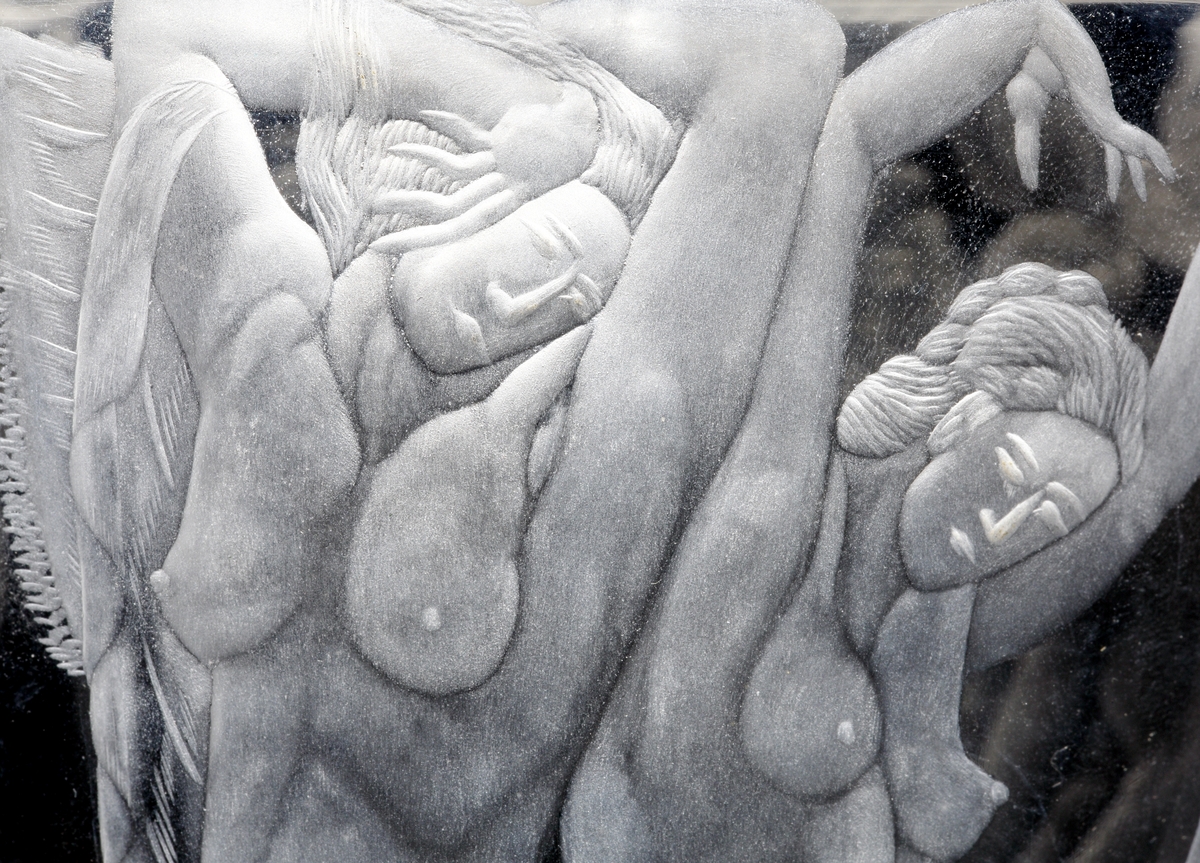 Design: Simon Gate. Graverad av Werner Abrahamsson (Orrefors 1926-46). Hög konisk vas som i botten avslutas med två vulster. Graverat motiv: Tre pilastrar med kapitäl avgränsar lika många fält, i vilka oklädda kvinnor figurerar i olika poser.