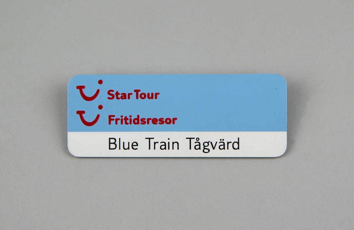 Rektangulär namnskylt av plast. Ljusblå och vit botten, "Star Tour" och "Fritidsresor" samt TUI:s logotyp i rött. "Blue Train Tågvärd" skrivet i svart. 
Svart baksida med säkerhetsnål. "RECOGNUS" i silver samt kontaktuppgifter till företaget.