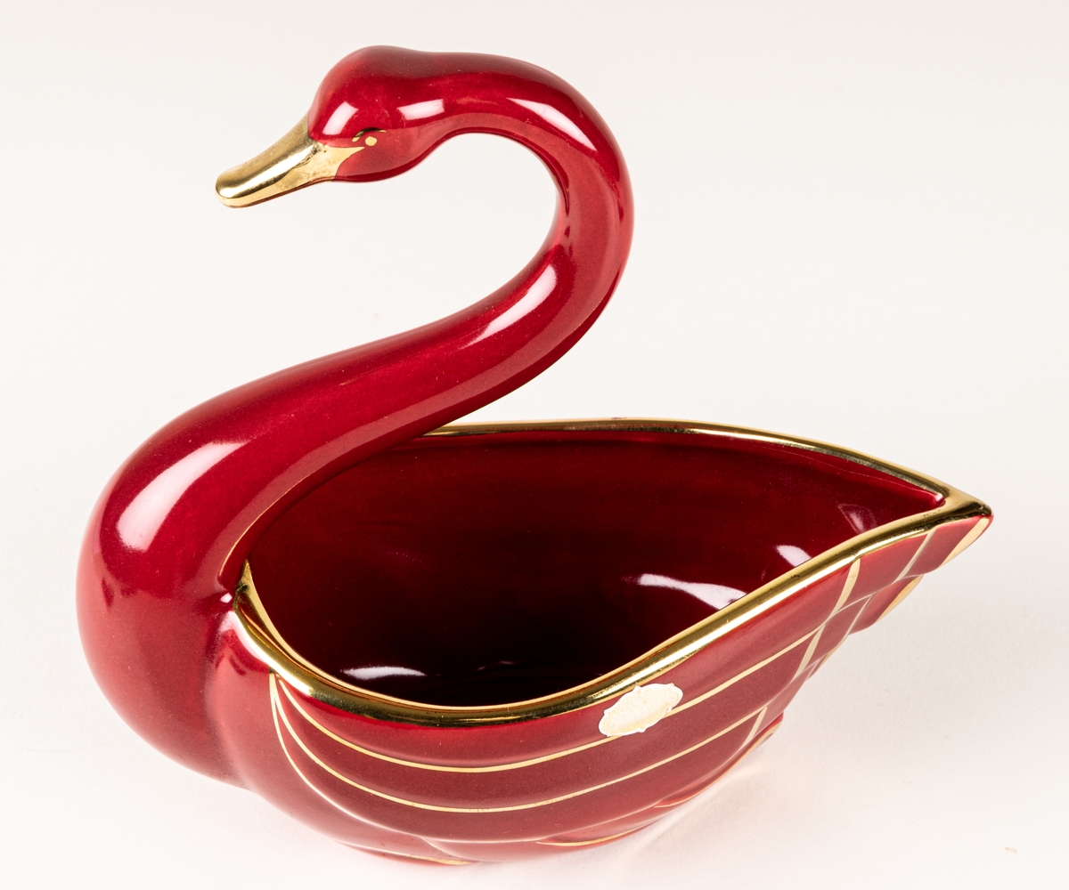 Prydnadsfigur eller skål i form av en svan, flintgods, modell A, dekorserie Rubin; röd glasyr med handmålat guld. Rubin producerades under åren 1940-1958. Oklart vem formgivaren är.