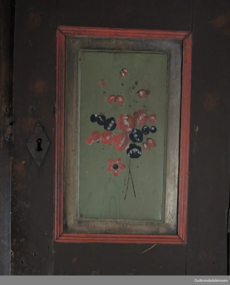 Todelt hjørneskap i malt tre med rosemalt dekor på dørspeil. Dørene er hengslet, tappet og har treplugger gjennom tappene; nøkkelhullslåser i begge dører. Overskapet har to hyller, festet med spiker. Nedre skapsdør er låst. Skapet er spikret til veggen.
Dekor i rokokkostil  med naturalistiske blomster. Kan være malt av  Rasmus Garmo fra Lom (1800-), treskjærer og rosemaler, elev av Per Veggum (1768-1836). Garmo malte ofte  naturalistiske blomster arrangert i fri grupper, ranker og empirevaser.