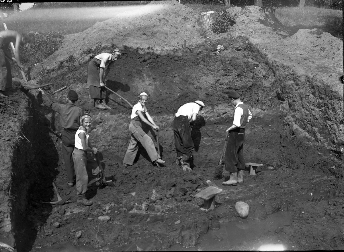 Utgrävning av schakt G på den sydvästra sluttningen av borgkullen vid Rumlaborg i Huskvarna sommaren 1942 pågår. På bilden syns deltagande elever från Huskvarna samrealskola.