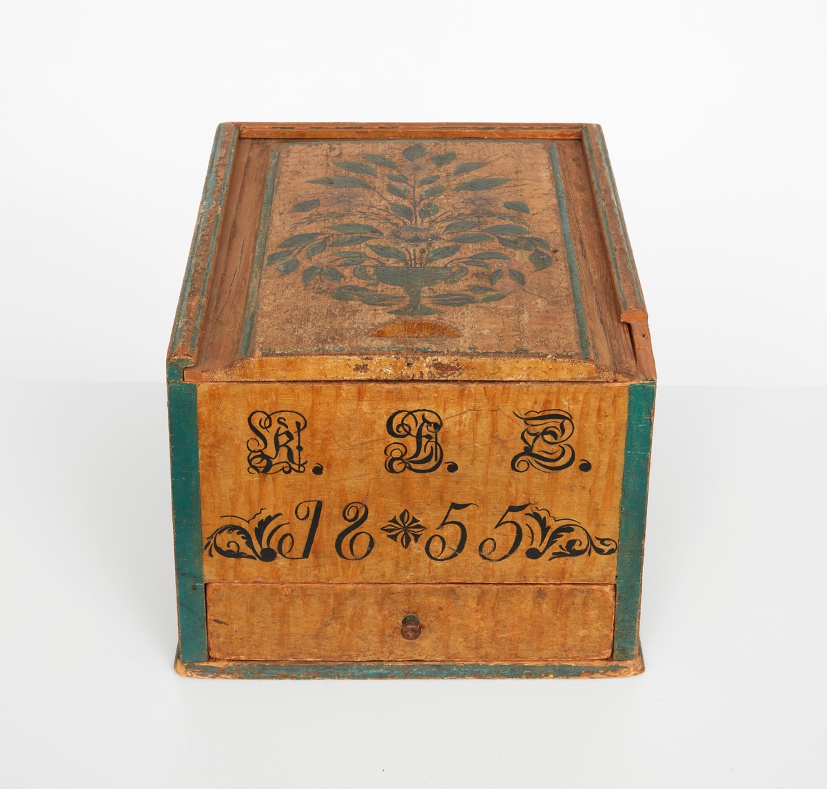 Timpask av furu, rektangulär med draglåda. Gulmålad med gröna hörn och lister. Draglock med blomsterurna i svart, grönt och vitt. Locket lagat på båda långsidorna. På askens kortsida: "K.B.D. ? 1855".