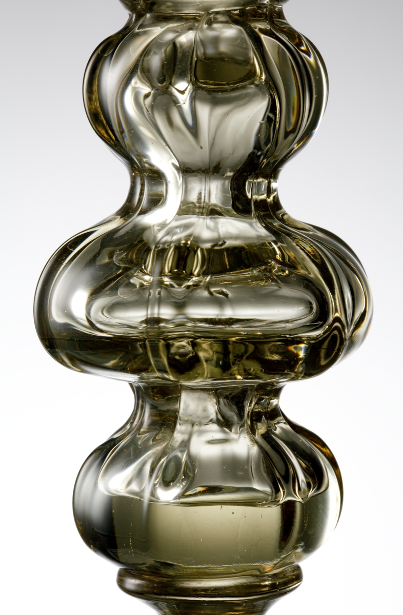 Formgivet av Simon Gate och tillverkat av mästare Knut Bergkvist. Pokal i venetiansk stil, svagt rosagulbruntonat glas. Räfflad kupa, räfflat ben med två inskärningar, som formar tre stycket "kulor".