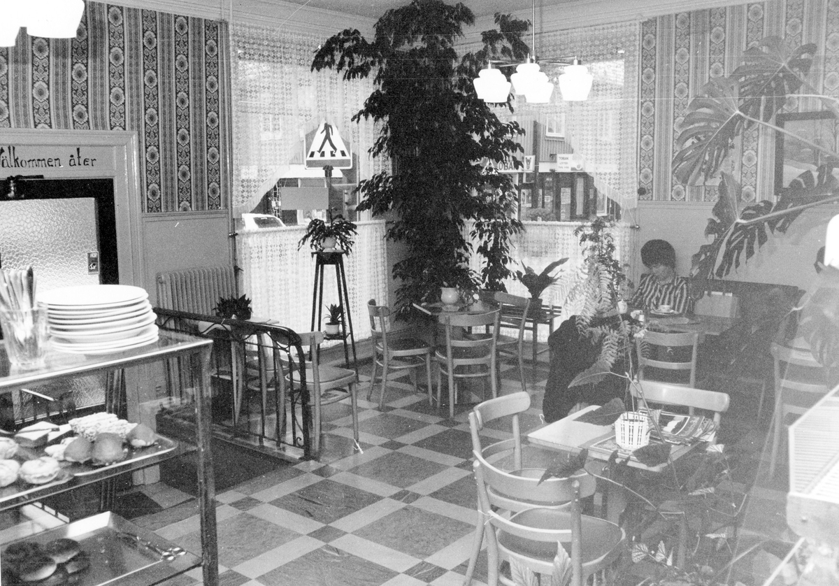 Café Hemtrevnad, hörnet Kungsgatan - Östra Ringgatan. Rörelsen startades på 1920-talet och lades ned vid årsskiftet 1980-81. En kvinna sitter och fikar i lokalen.