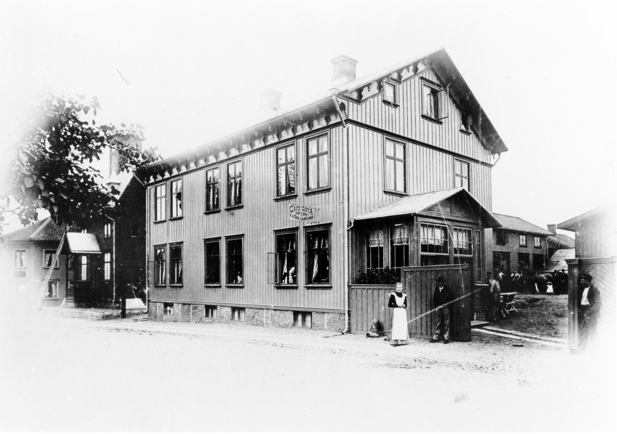 Gatuvy av Café Göta när det låg på Nygatan, kv. Färgaren 5, mellan 1889-1930. Caféet låg på första våningen, vid ingången står en kvinna i förkläde samt två män. På innegården syns människor samt en häst. En skylt på fasaden med text "Café Göta Servering Kaffe & Läskedrycker". Sedan flyttade verksamheten till Norra Strömgatan, kv. Färgaren 4.