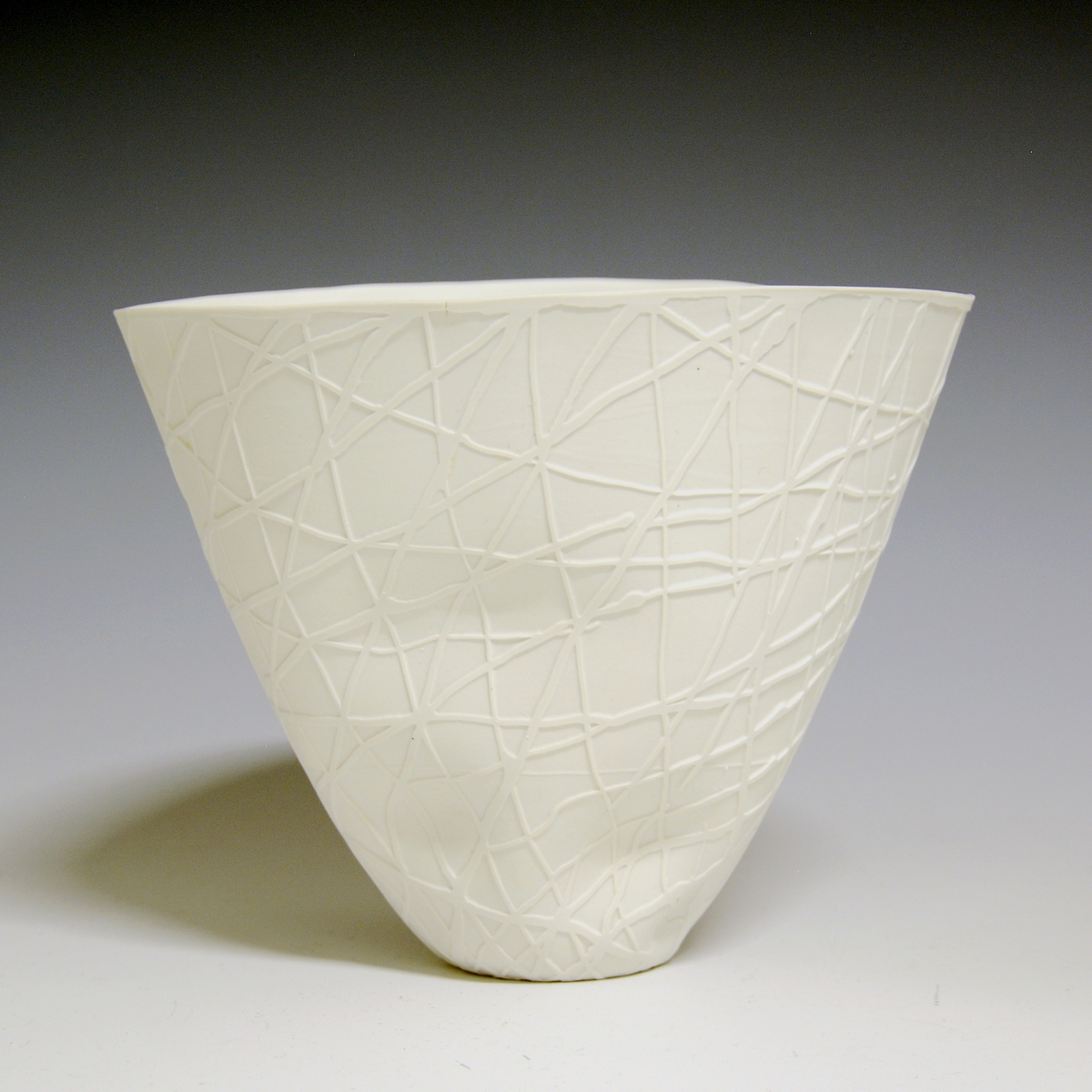 Vase av porselen, hvit uglasert. Smal bunn, skråner utover i en vid åpning. Sandblåst dekor. Dekorert i råbrent tilstand med flytende latex, sandmattet. Latexen fjernet før høybrenning.
