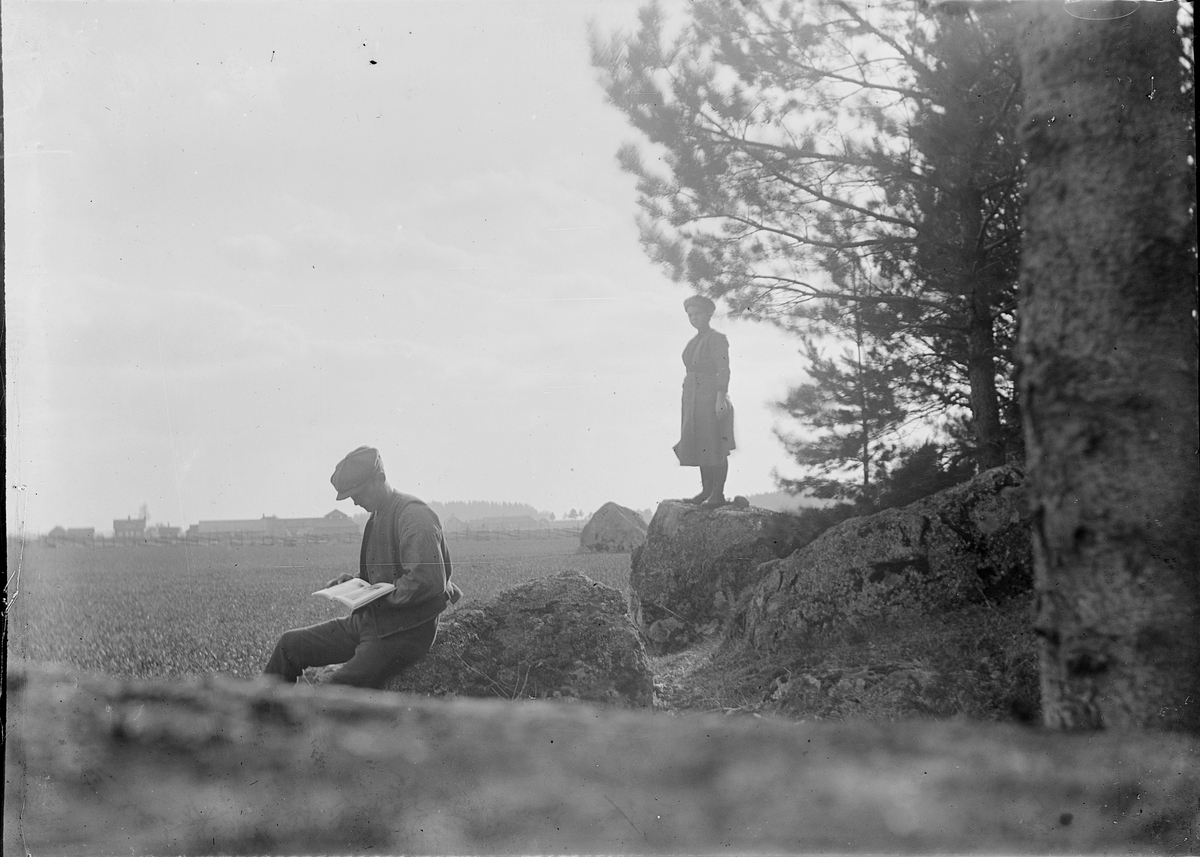 Man sitter på sten och läser, kvinna står på sten i bakgrunden