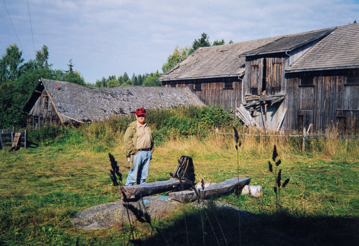 Bildet fra gårdstunet på Stensåsen gård i Løten. Bilde viser fjøset og låven i Stensåsen. Og er tatt ved en kafferast i 1998. Ivar Stensåsen står ved kvilebenken. Foto: Eva Stensåsen, Privat eie.