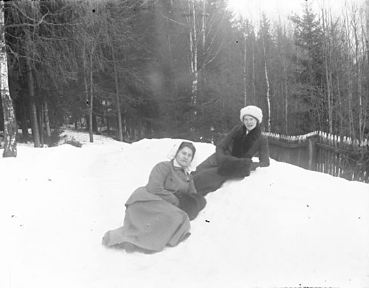 Grupporträtt, två kvinnor i vinterkläder och muff, vilande i snön.