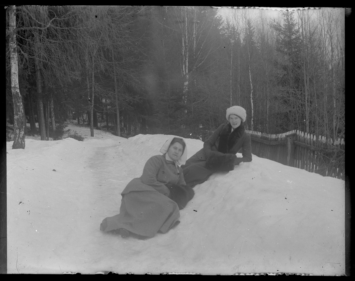 Grupporträtt, två kvinnor i vinterkläder och muff, vilande i snön.