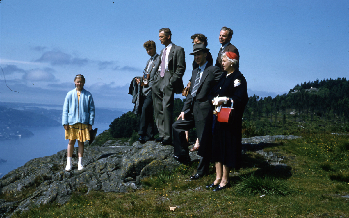 Gruppebilde pent kledde mennesker på en knaus over en fjord
