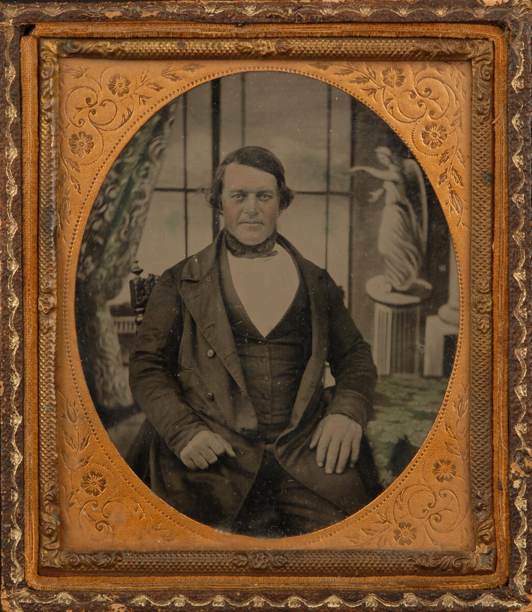 Bildet viser et sort-hvitt portrett av en pent kledd mann. Fotografiet er inne i en forseggjort gylden ramme.