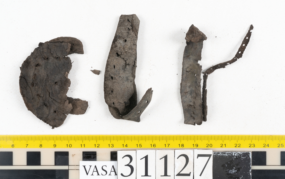 Delar och fragment från sko; tre sulor, en holtrand, en klacklapp, en klacklapp eller ett inlägg samt ett 40-tal delar och mindre fragment från skoöverdel och skobotten.
Sula fyndnummer 31127 har kvarsittande tråd. På sulans ovansida finns intryck av bindtråden.  Sula fyndnummer 31127:1 har kvarsittande träpligg och tråd. I tåpartiet finns en laglapp. Sulans hälparti är avskuret, eventuellt avbrutet.  Sula fyndnummer 31127:2 har ett fragmentariskt hälparti. På sulans ovansida finns intryck av bindtråd. Holtrand fyndnummer 31127:3 har kvarsittande tråd. På klacklapp fyndnummer 31127:4 finns hål efter träpligg. På klacklapp, eventuellt inlägg, fyndnummer 31127:5 finns kvarsittande tråd.