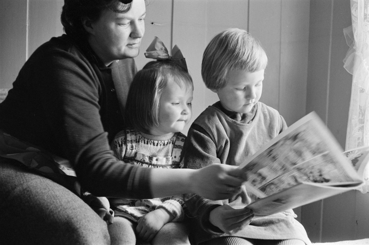 En kvinne leser et blad med to barn.
