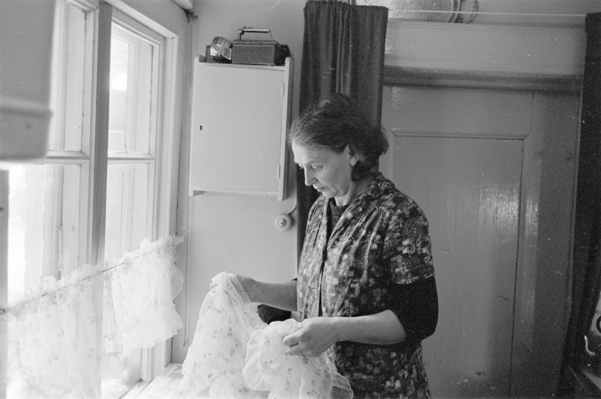En kvinne henger opp gardiner i et kjøkken på Røros.