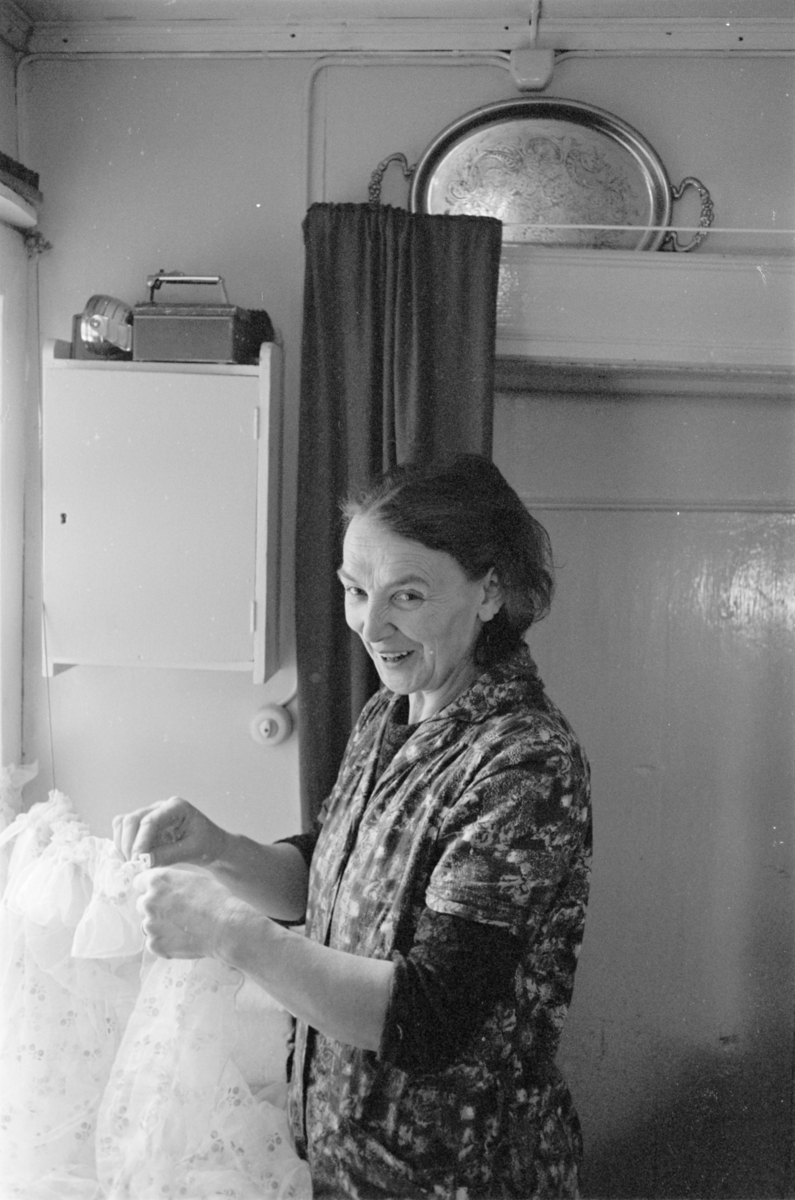 En kvinne henger opp gardiner i et kjøkken på Røros.