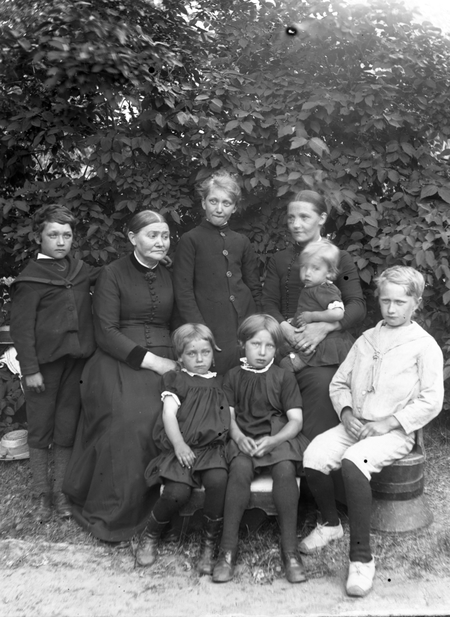 Jensine Anundsen t.v. med en kvinne og åtte barn. Løvverk i bakgrunnen, Berg.