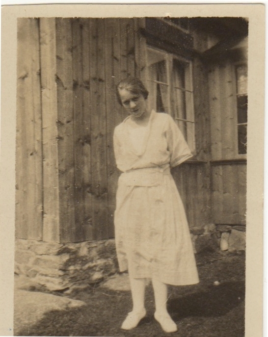 Troligtvis konfirmation för "Lisa" Elise Ingeborg Olsson (född 1898 i Torp, Uddevalla, senare boende i Myckleby) står framför ett trähus 1912-1913. Gift med Axel Johansson, Labacka 1:2 "Lund".