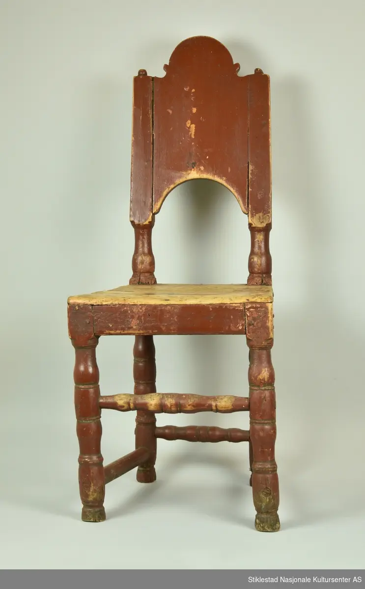 Stol i tre med høy rygg. Ryggbrett felt inn i sidestolper. Dreide føtter. 
, såkalt Verdalsstol. Høy og hel rygg, rødbrun i fargen. Dreide, liggende stolper nederst på føtter, montert i samme høyde (bak og på stolens sider). Foran er den dreide stolpen monter noe høyere opp. Ryggbrettet har en buet form, sidestolper med dreide kuler på toppen. Stolen er malt i en rødbrun farge. Malingen er slitt bort fra sete.
